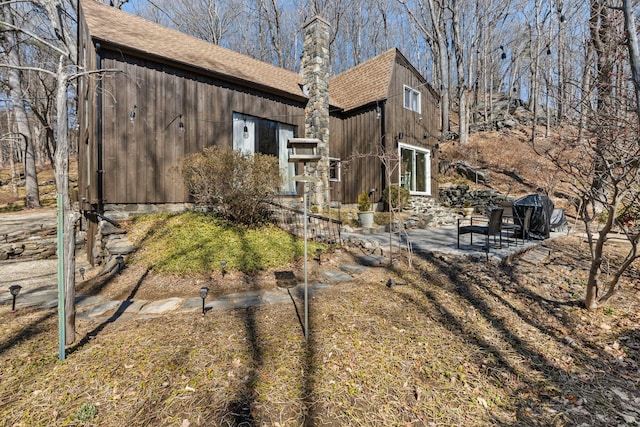 view of home's exterior featuring a chimney, a patio, and a shingled roof