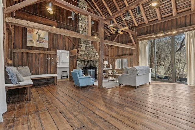 unfurnished living room with a stone fireplace, hardwood / wood-style flooring, wooden walls, and high vaulted ceiling