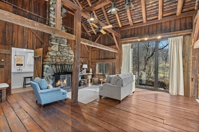 unfurnished living room with wood-type flooring, high vaulted ceiling, a stone fireplace, and wooden walls