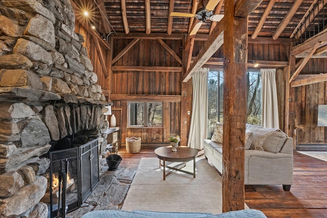 unfurnished living room featuring wooden walls, a stone fireplace, a towering ceiling, a ceiling fan, and wood-type flooring