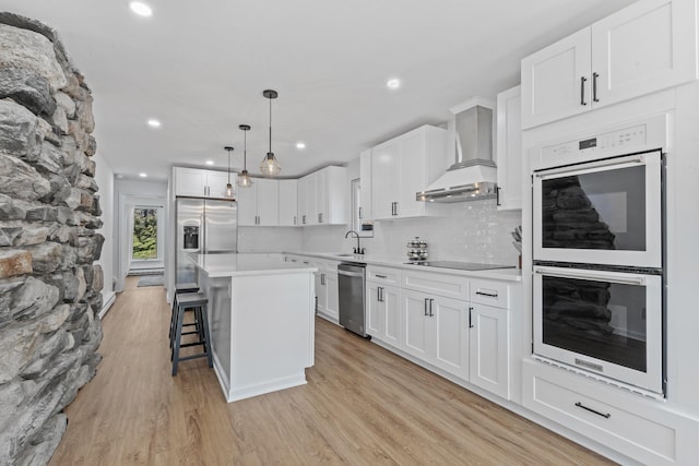 kitchen with wall chimney range hood, stainless steel fridge with ice dispenser, double oven, light countertops, and light wood-style floors