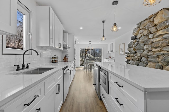 kitchen with backsplash, appliances with stainless steel finishes, wood finished floors, white cabinetry, and a sink