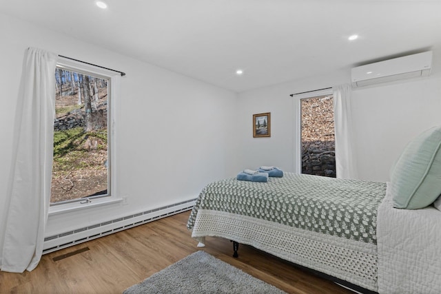 bedroom with multiple windows, wood finished floors, a wall mounted AC, and a baseboard radiator