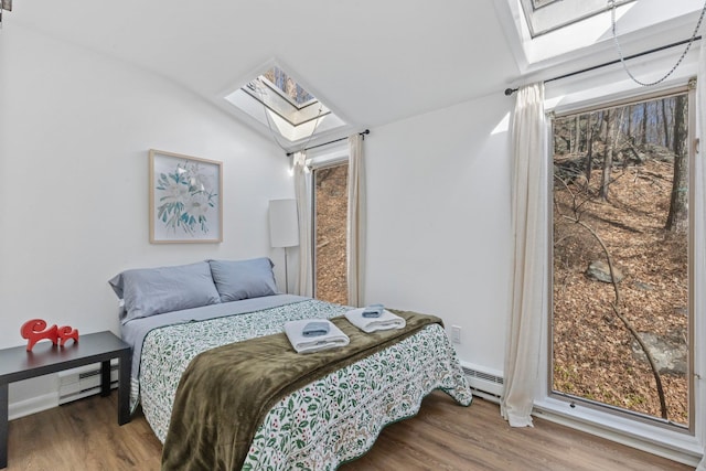 bedroom featuring a baseboard heating unit, multiple windows, wood finished floors, and vaulted ceiling with skylight