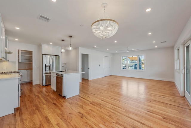 kitchen featuring visible vents, an island with sink, open floor plan, decorative light fixtures, and white cabinetry