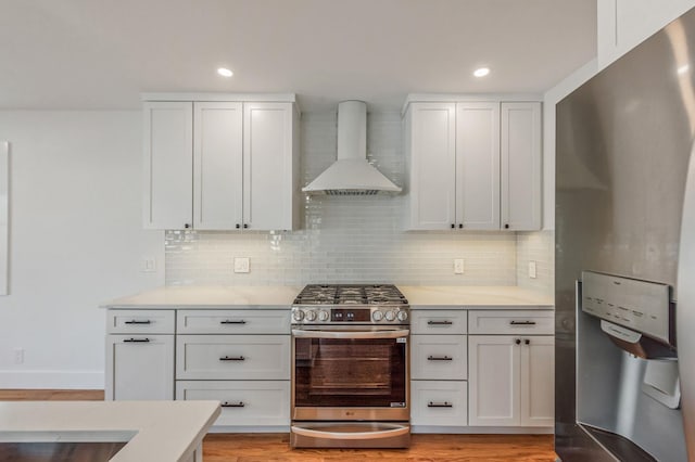 kitchen with stainless steel appliances, white cabinetry, light countertops, wall chimney range hood, and backsplash