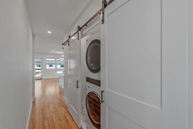 laundry area with stacked washer and clothes dryer, a barn door, light wood-style floors, laundry area, and baseboards