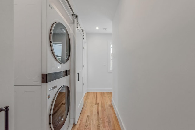 washroom with laundry area, a barn door, baseboards, stacked washer and clothes dryer, and light wood-style flooring