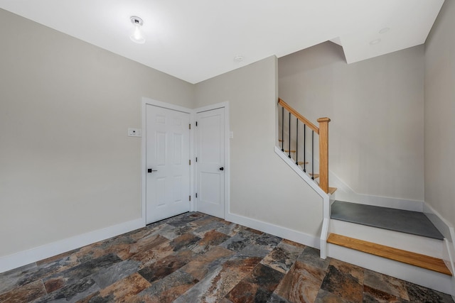 foyer with stone finish floor, stairway, and baseboards