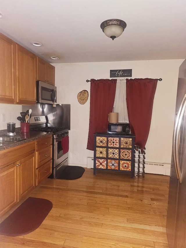 kitchen featuring dark countertops, appliances with stainless steel finishes, brown cabinets, baseboard heating, and light wood-type flooring