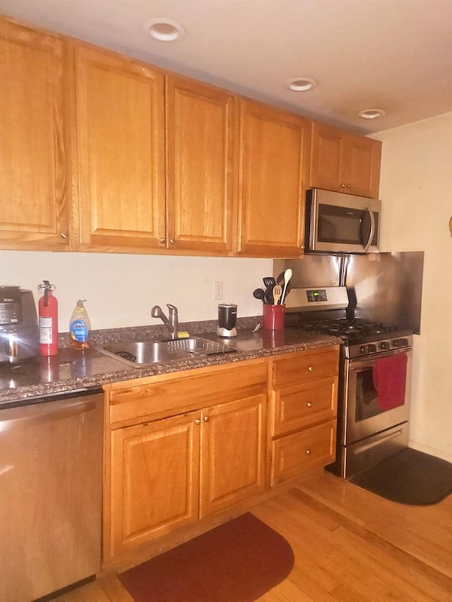 kitchen with stainless steel appliances, light wood-style floors, dark stone counters, and a sink