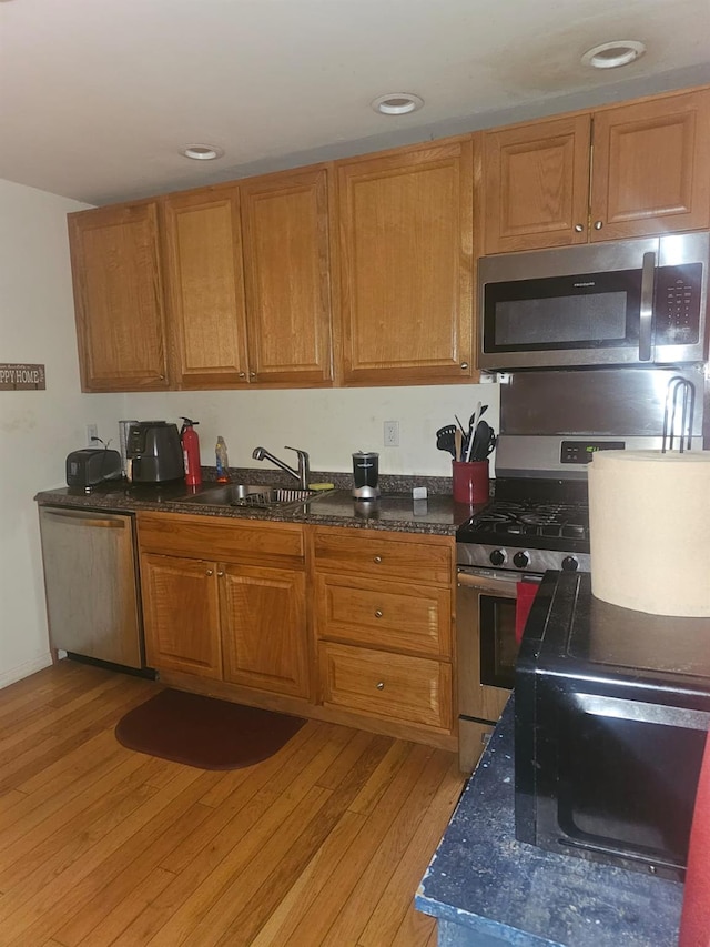 kitchen featuring stainless steel appliances, dark countertops, light wood-style floors, brown cabinetry, and a sink