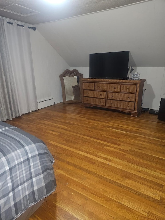 bedroom with a baseboard radiator, wood finished floors, and lofted ceiling