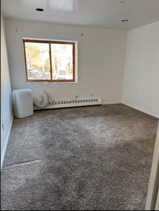 spare room featuring a baseboard heating unit, carpet, and baseboards