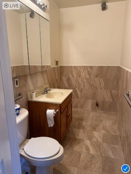 half bathroom featuring wainscoting, tile walls, toilet, and vanity