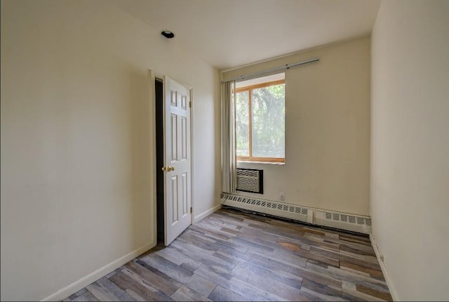 unfurnished room with baseboard heating, wood finished floors, and baseboards