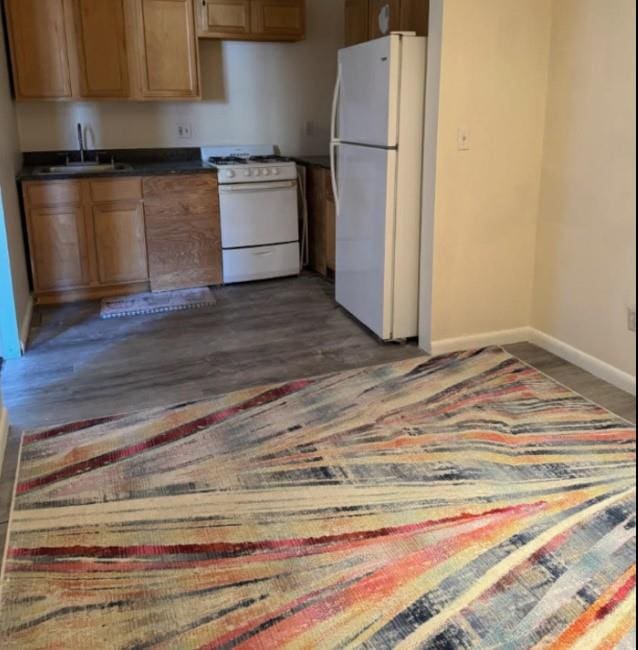 kitchen with white appliances, baseboards, dark countertops, dark wood-type flooring, and a sink