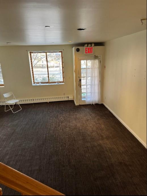 unfurnished room with a baseboard radiator, baseboards, and dark colored carpet