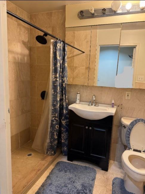 118-82 Metropolitan Ave Unit 1B, Kew Gardens, NY 11415 - full bath with a shower stall, toilet, vanity, tile patterned floors, and tile walls