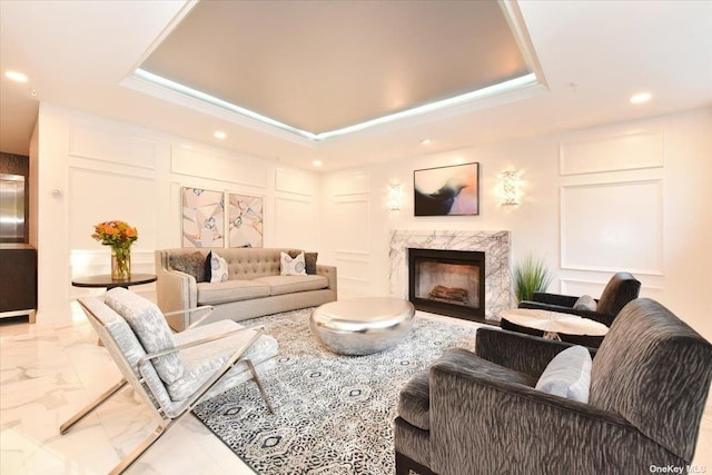 living room featuring a decorative wall, marble finish floor, and a tray ceiling