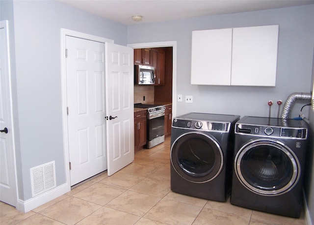 laundry area with light tile patterned floors, cabinet space, baseboards, visible vents, and washing machine and clothes dryer