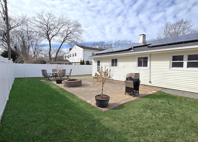 rear view of house featuring a fenced backyard, a fire pit, a yard, a chimney, and a patio area