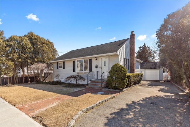 view of front of house featuring driveway, a chimney, a detached garage, an outbuilding, and fence