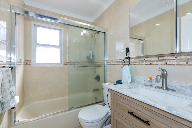 bathroom with toilet, vanity, tile walls, ornamental molding, and combined bath / shower with glass door