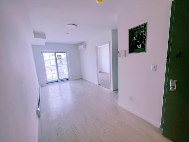 spare room with a wall mounted AC, light wood-type flooring, a baseboard radiator, and baseboards