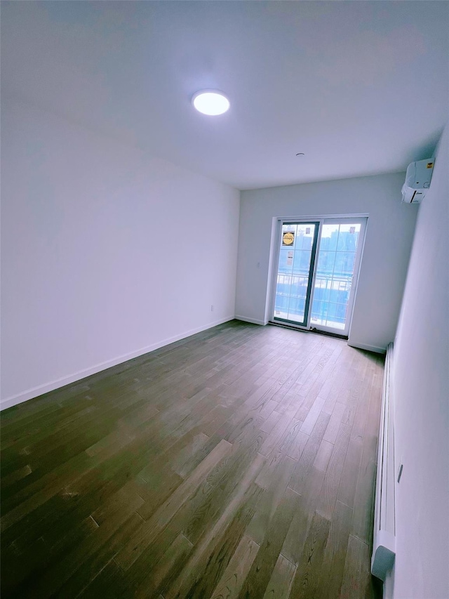 empty room with dark wood-style floors, baseboards, and a wall mounted AC