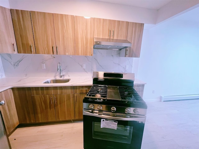 kitchen featuring a sink, wall chimney range hood, tasteful backsplash, brown cabinetry, and gas range