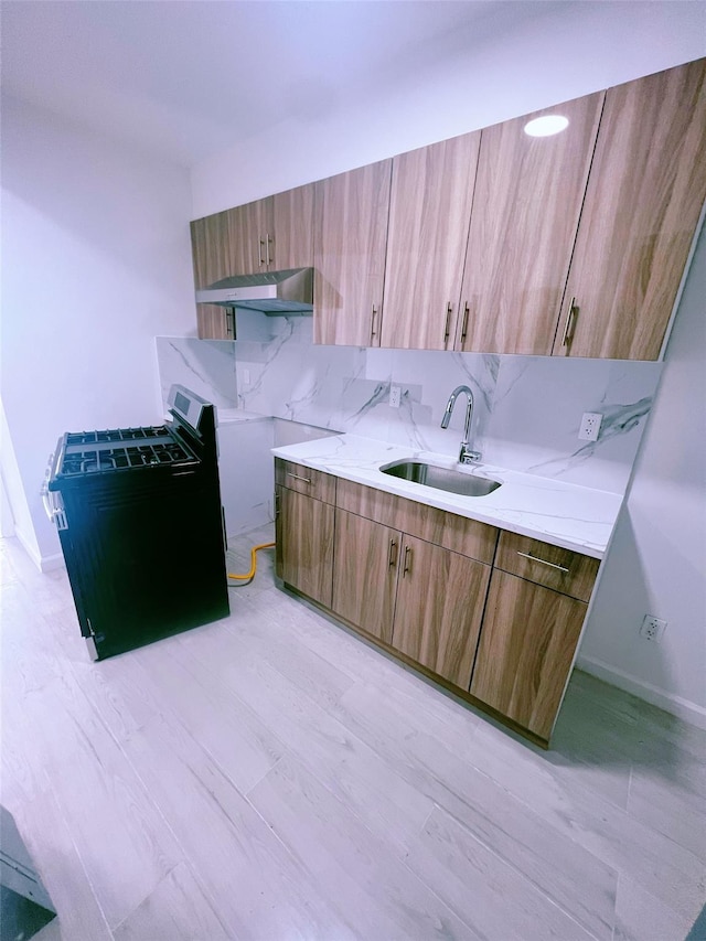 kitchen with decorative backsplash, brown cabinetry, light wood-type flooring, under cabinet range hood, and a sink