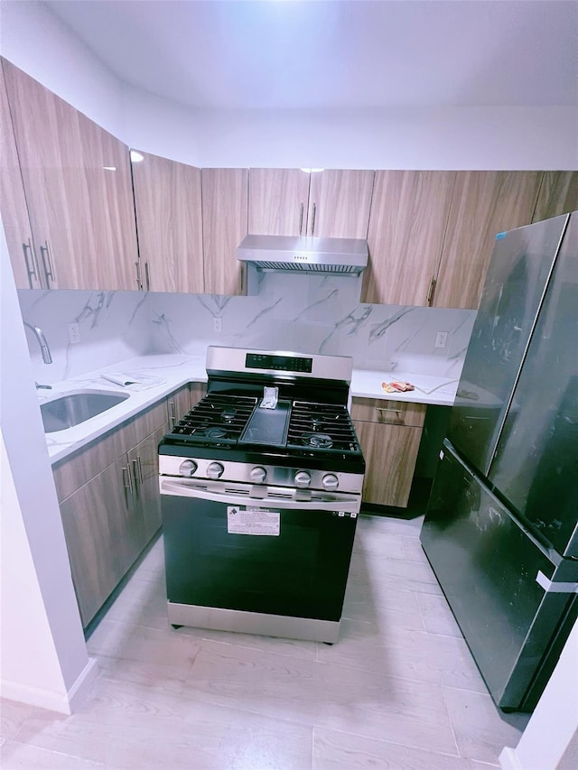 kitchen featuring range hood, light countertops, freestanding refrigerator, a sink, and stainless steel gas range