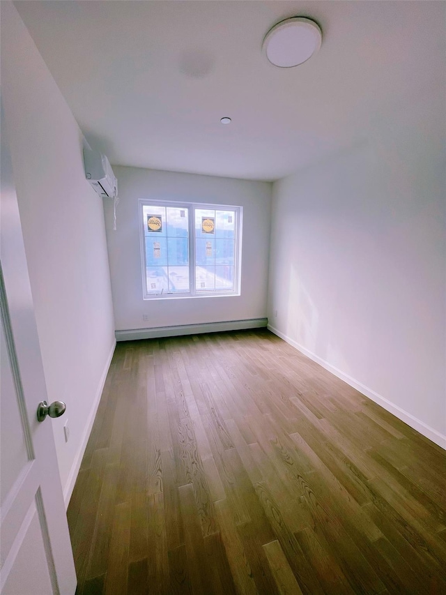 unfurnished room featuring baseboards, a wall unit AC, baseboard heating, and wood finished floors