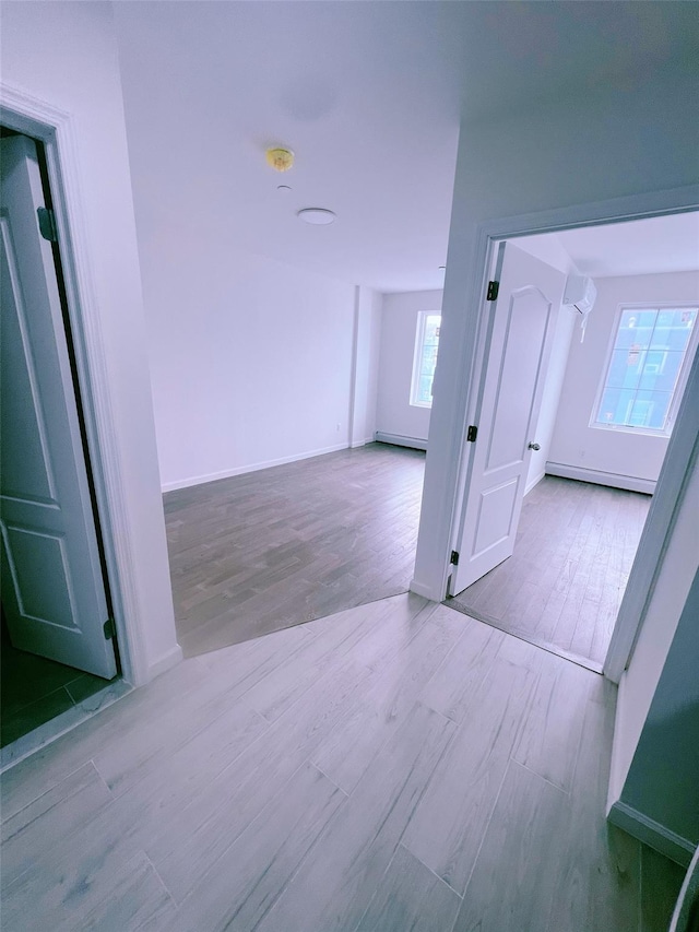 interior space with a baseboard heating unit, light wood-type flooring, and baseboards