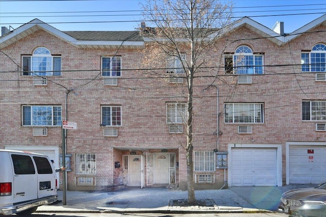 view of front of property with an attached garage, a wall mounted AC, and brick siding