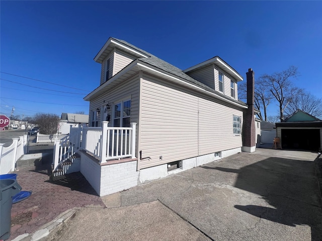 view of property exterior with an outdoor structure, driveway, a detached garage, and fence