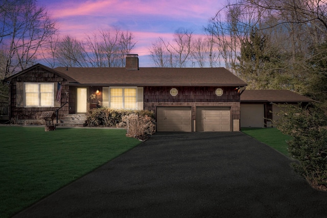 view of front facade featuring a yard, aphalt driveway, a chimney, and an attached garage