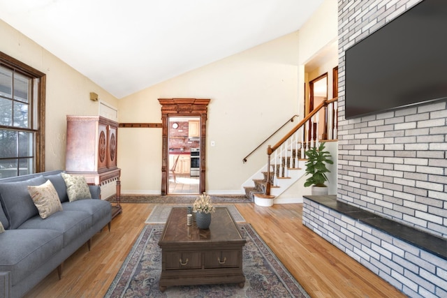 living room featuring high vaulted ceiling, stairway, baseboards, and wood finished floors