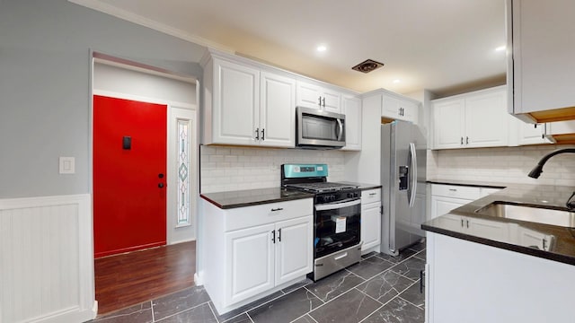 kitchen featuring a sink, white cabinetry, marble finish floor, appliances with stainless steel finishes, and wainscoting