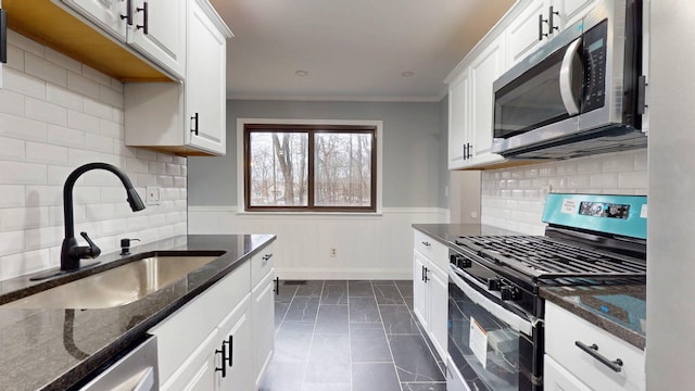 kitchen featuring stainless steel appliances, wainscoting, a sink, and white cabinets