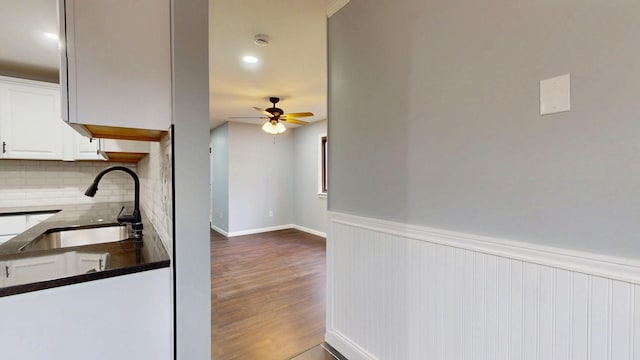 kitchen featuring a wainscoted wall, dark wood-type flooring, a sink, white cabinetry, and dark countertops