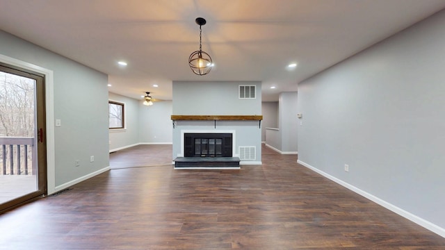 unfurnished living room with dark wood-style floors, a glass covered fireplace, visible vents, and baseboards