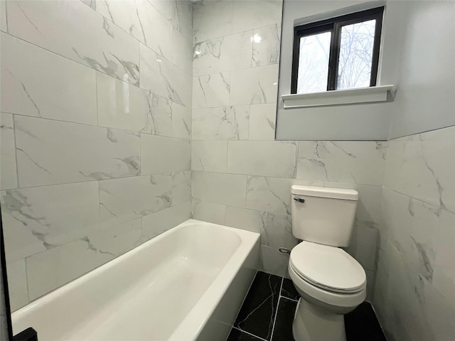 bathroom with toilet, marble finish floor, a bathtub, and tile walls