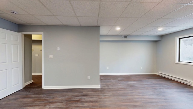 empty room featuring a baseboard heating unit, visible vents, wood finished floors, and a paneled ceiling