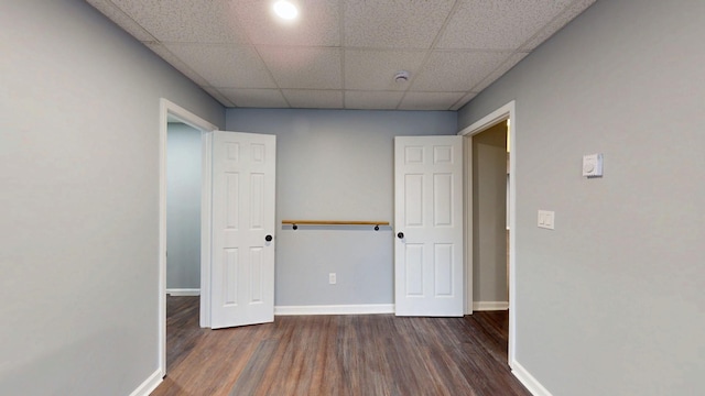 unfurnished bedroom with wood finished floors, a paneled ceiling, and baseboards