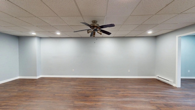 below grade area with ceiling fan, a paneled ceiling, a baseboard heating unit, baseboards, and dark wood finished floors