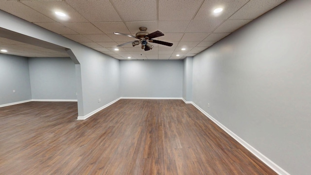 basement featuring arched walkways, wood finished floors, a ceiling fan, and baseboards