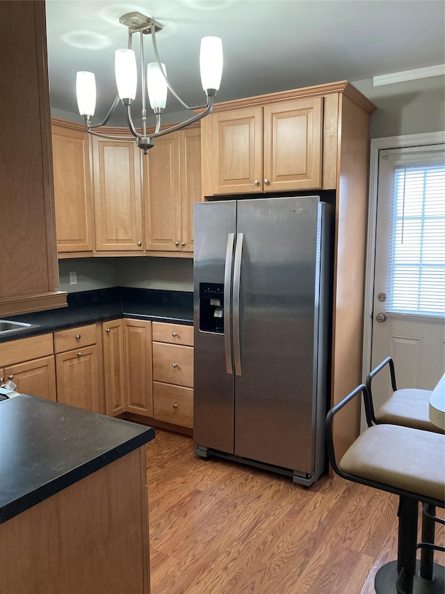 kitchen featuring light wood finished floors, dark countertops, stainless steel fridge, and decorative light fixtures