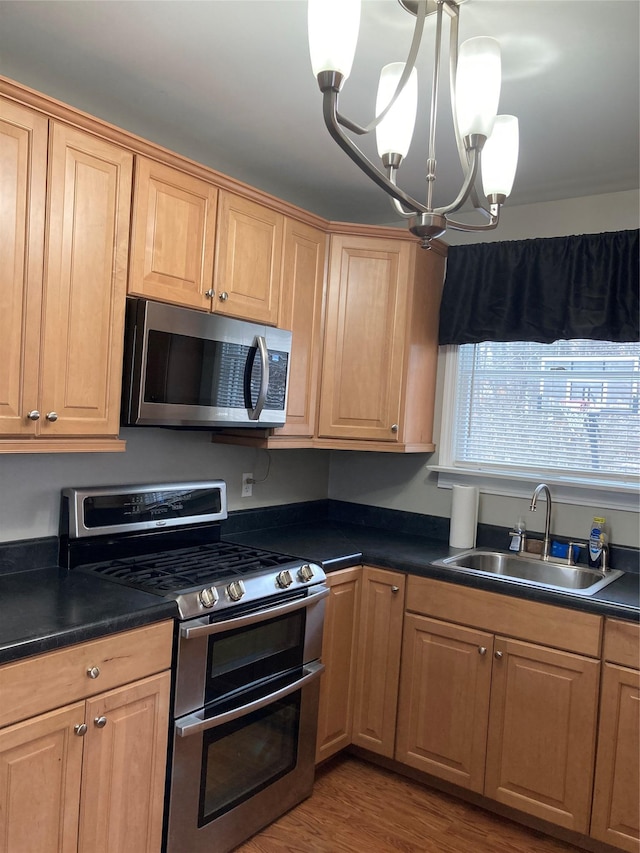 kitchen featuring dark countertops, light wood-style flooring, decorative light fixtures, stainless steel appliances, and a sink